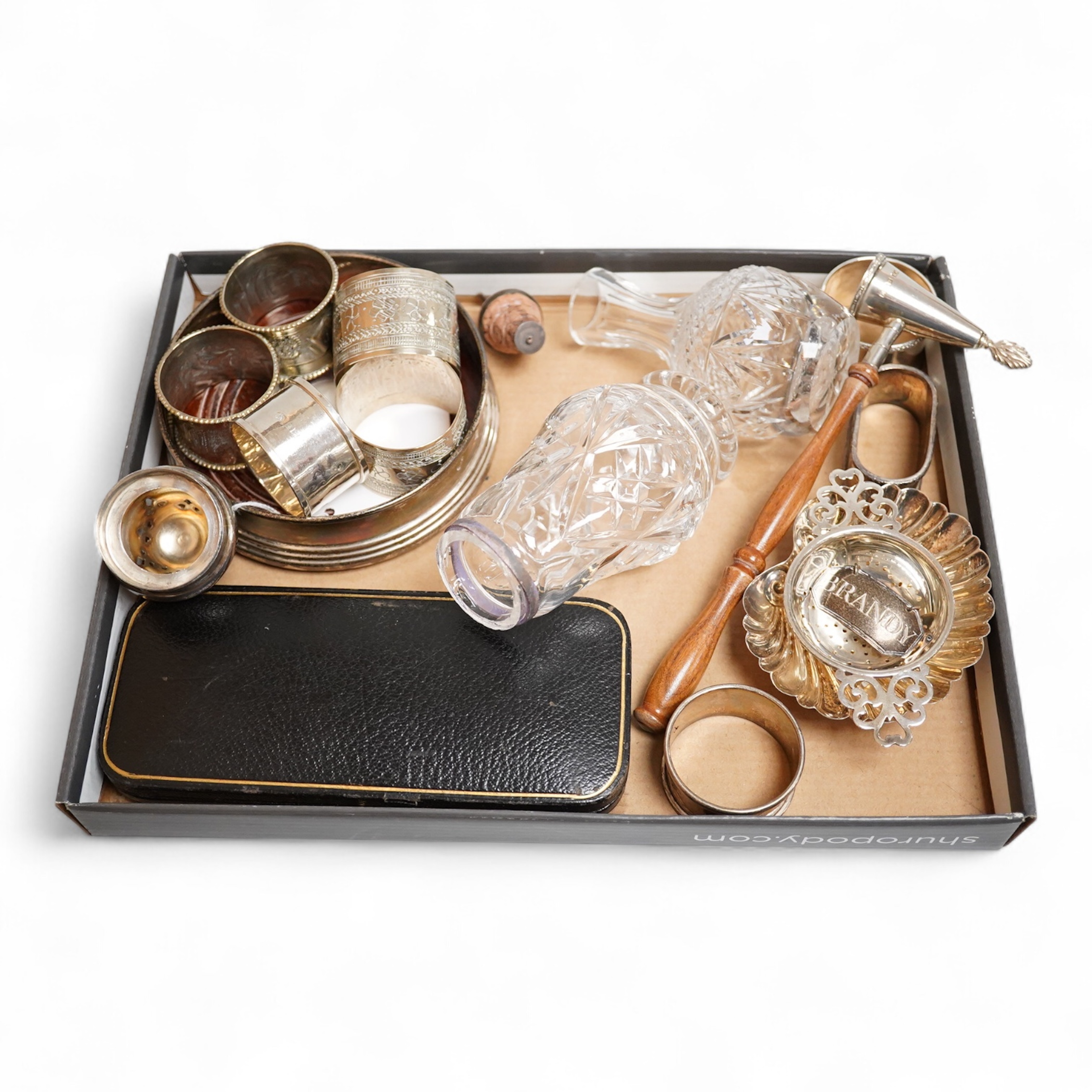 A modern silver mounted wine coaster, diameter 12cm, four silver napkin rings, four continental white metal napkin rings, a modern silver candle extinguisher, a silver tea strainer, small 925 shell dish, a George III sil